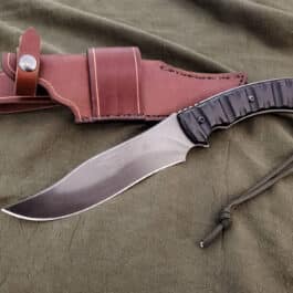 A HANDMADE LEATHER SHEATH FOR THE TOPS LONGHORN BOWIE laying on a bed.