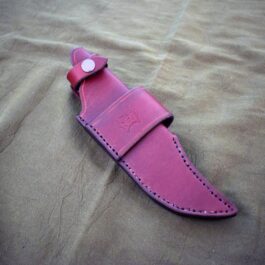 A pink handmade leather sheath for the TOPs Longhorn Bowie knife laying on a bed.