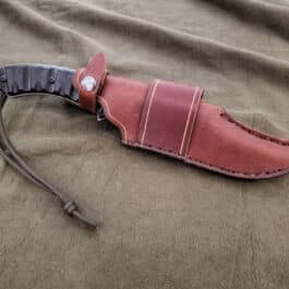 A TOPs Longhorn Bowie with a Handmade Leather Sheath on a bed.