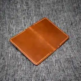 A handmade leather passport wallet sitting on top of a gray cloth.