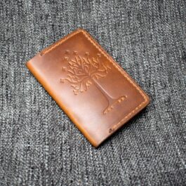 A handmade leather passport wallet sitting on top of a gray cloth.