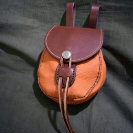 A brown and tan Small Sporran Belt Pouch laying on a bed.