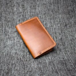A handmade leather passport wallet sitting on top of a gray cloth.