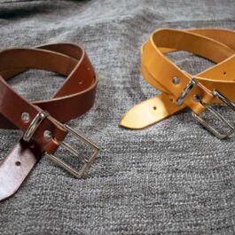 A handmade leather dress belt sitting on top of a bed.