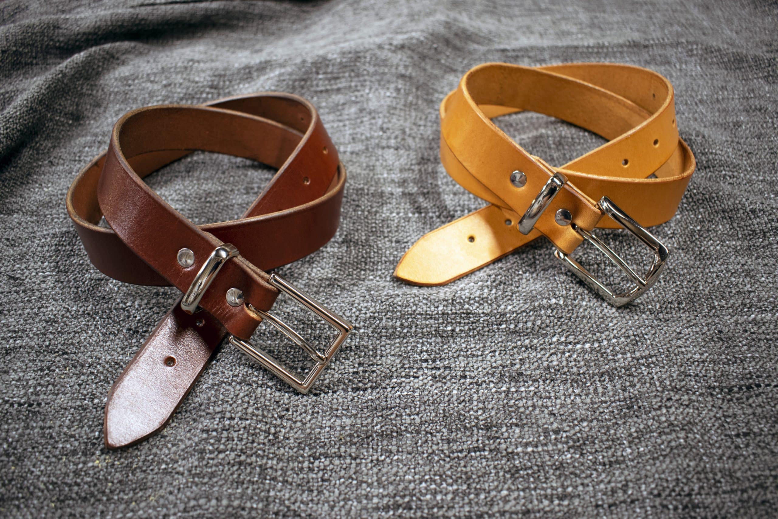A handmade leather dress belt sitting on top of a bed.