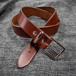 A Handmade Leather Dress Belt is laying on a gray cloth.