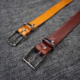 A pair of Handmade Leather Dress Belts sitting on top of a carpet.