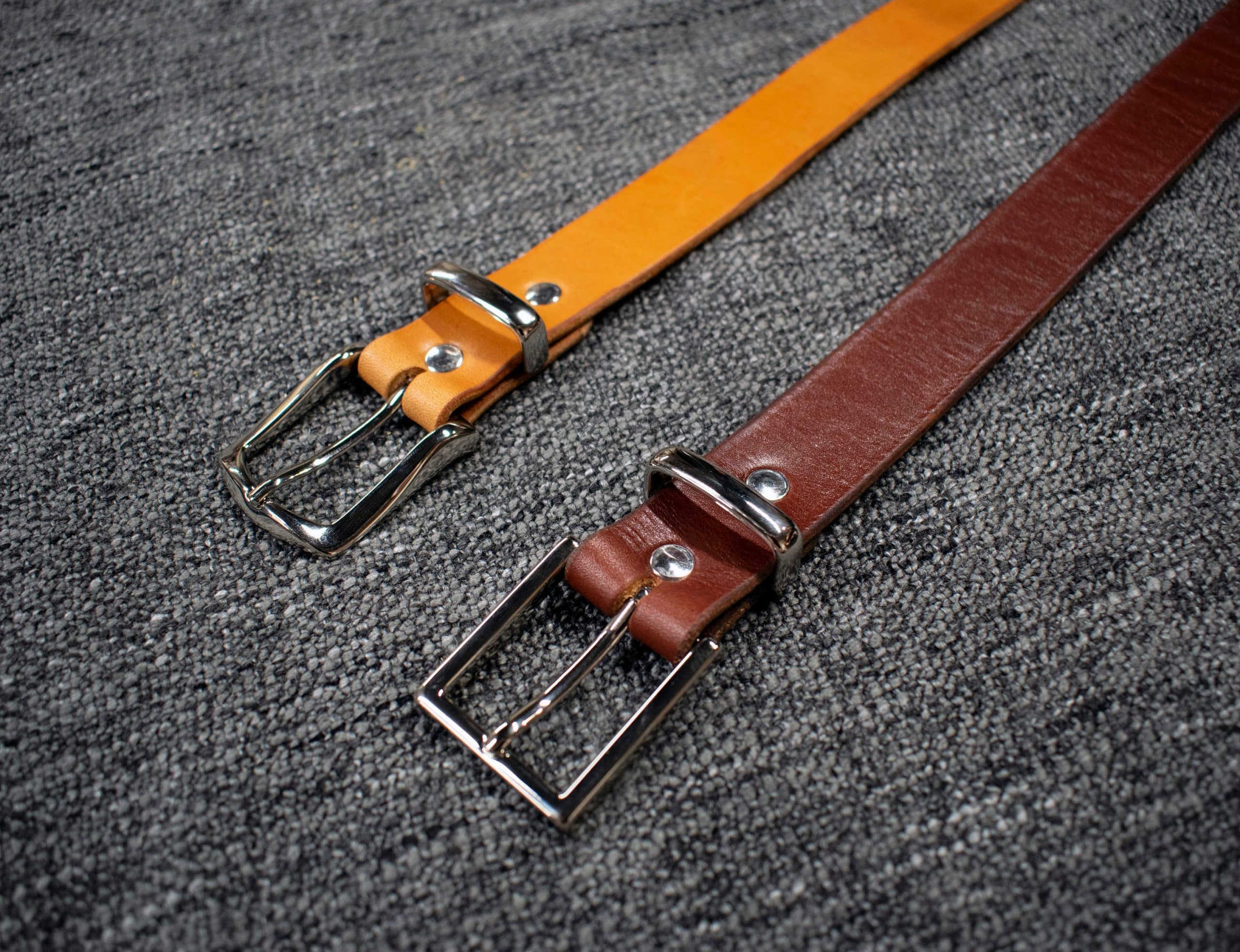 A pair of Handmade Leather Dress Belts sitting on top of a carpet.