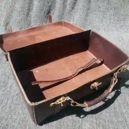 A handmade leather suitcase sitting on top of a gray carpet.
