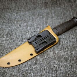 A Kydex Sheath for the Ka Bar Fighting Knife that is laying on the ground.