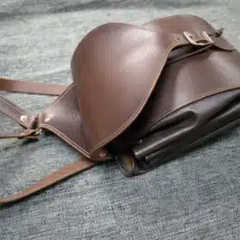 A brown Leather Cinch Top Backpack sitting on top of a bed.