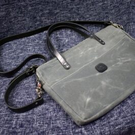 A Waxed Canvas Briefcase Satchel sitting on top of a blue couch.
