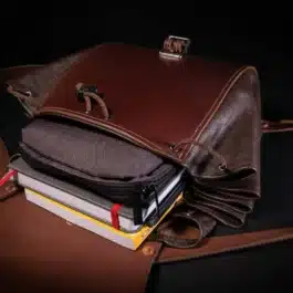 A Leather Cinch Top Backpack sitting on top of a pile of books.