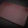 A brown leather Handmade Leather Mouse Pad on a black surface.