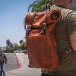 A man with a Bison Leather Roll Top Rucksack walking down a street.