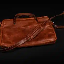 A bison leather briefcase satchel sitting on top of a black table.