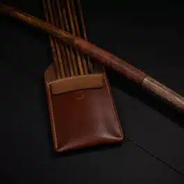 A brown Leather Pocket Quiver sitting next to a wooden stick.