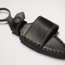 A Handmade Leather Sheath for the Benchmade Mini SOCP Dagger is laying on a black leather case.