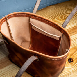 A Horween Leather Tote Bag sitting on top of a wooden floor.