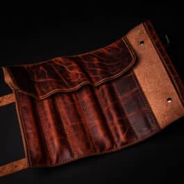 A Handmade Leather Pen Roll with a belt on a black background.