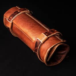 A handmade leather pen roll sitting on top of a black surface.
