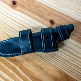 A black Leather Sheath for the Benchmade Fixed Contego sitting on a wooden table.