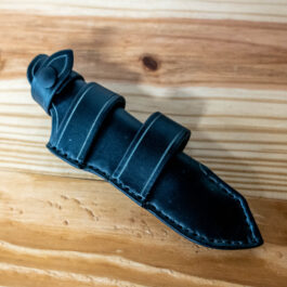 A black Leather Sheath for the Benchmade Fixed Contego sitting on a wooden table.