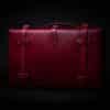 A red Handmade Leather Suitcase sitting in the dark.