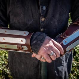 A man in a black jacket holding Splinted Vambraces with brown and silver details.