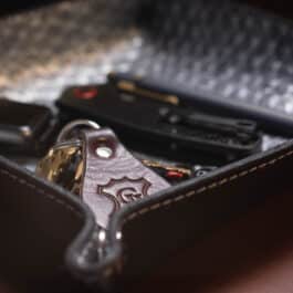 A Blue Mythical Koi Suede Lined Valet Tray filled with cell phones on top of a table.