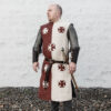 a man wearing a burgundy and cream linen surcoat with crosses on the front