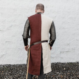 a man wearing a burgundy and cream linen surcoat with crosses on the front