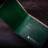 An Emerald Green Shell Cordovan Bifold Wallet sitting on top of a brown leather surface.
