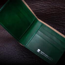 An Emerald Green Shell Cordovan Bifold Wallet sitting on top of a brown leather surface.