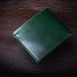 An Emerald Green Shell Cordovan Bifold Wallet sitting on top of a brown leather surface.