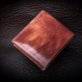 An Emerald Green Shell Cordovan Bifold Wallet sitting on top of a black leather surface.