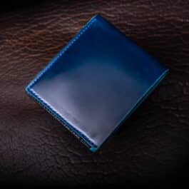 An Emerald Green Shell Cordovan Bifold Wallet sitting on top of a brown leather surface.