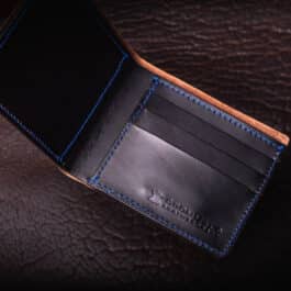 An Emerald Green Shell Cordovan Bifold Wallet on a brown leather surface.