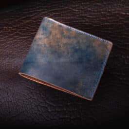 An Emerald Green Shell Cordovan Bifold Wallet sitting on top of a leather surface.