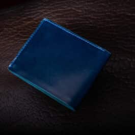 An Emerald Green Shell Cordovan Bifold Wallet sitting on top of a brown leather surface.