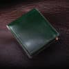 An Emerald Green Shell Cordovan Bifold Wallet sitting on top of a brown leather surface.