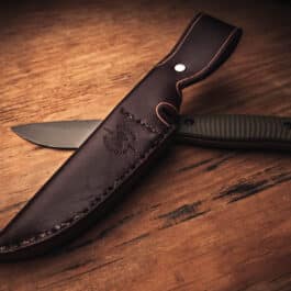 A Benchmade Anonimus knife with a Handmade Leather Sheath on a wooden table.