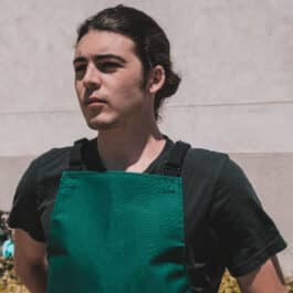A man with a canvas apron standing in front of a building.