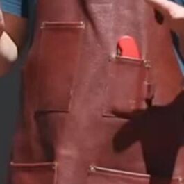 A man wearing a brown leather Custom Apron holding a cell phone.
