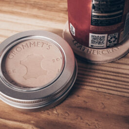 a metal tin filled with round leather coasters next to an aluminum can on top of a coaster