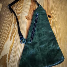 a green leather sling bag on a wooden table