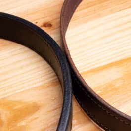 A black Leather belt next to a brown leather belt on a wooden table