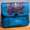 a blue leather bag with rainbow accents sitting on a wooden table
