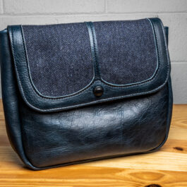 a blue leather bag with blue wool inlay sitting on a wooden table