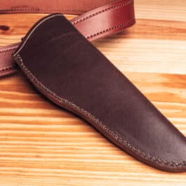 A handmade leather sheath sitting on top of a wooden table.